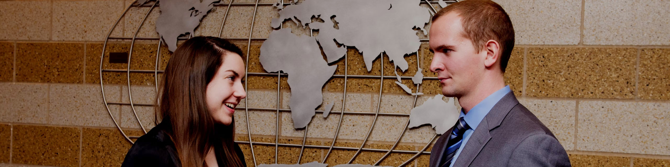 Two students talking in front of a globe mural inside of a building